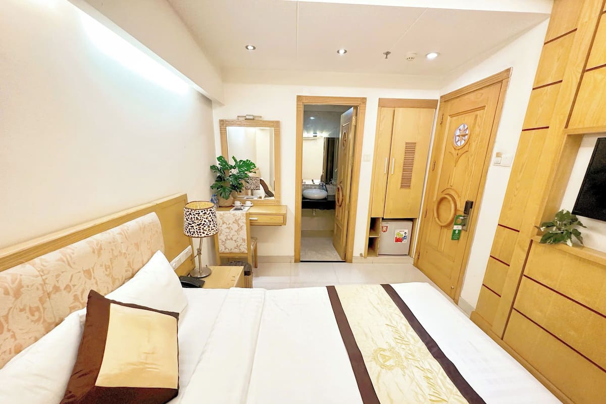 Una habitación de hotel con cama, mesita de noche, lámpara, cómoda, espejo y una puerta que da al baño.