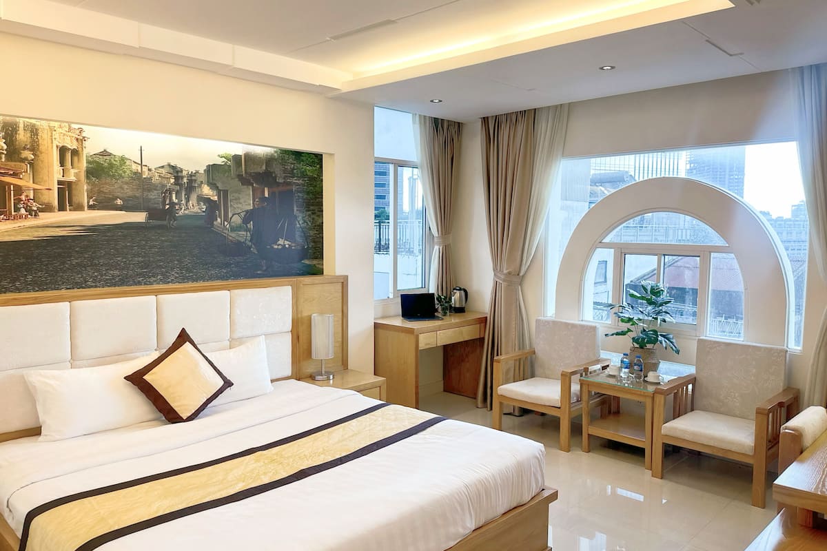 Habitación de hotel con una cama grande, un escritorio, una silla, una mesita y una ventana con vistas a edificios.