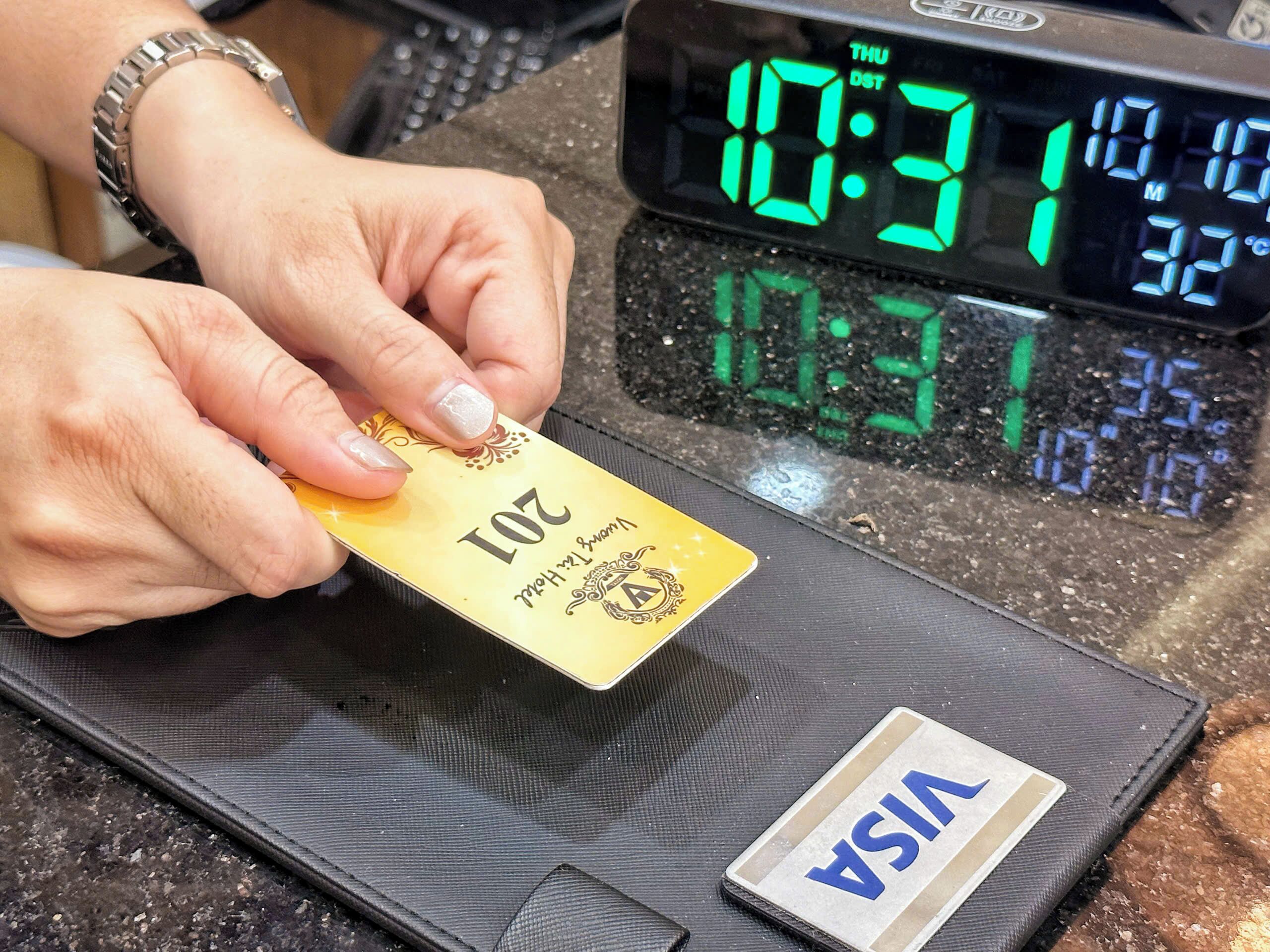 A person holding a card near a digital scale with a VISA label, and a digital clock displaying 10:31.