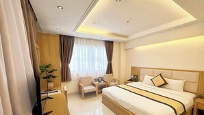 Une chambre d’hôtel avec un grand lit, un bureau avec une chaise, une petite table avec une lampe et une plante en pot.