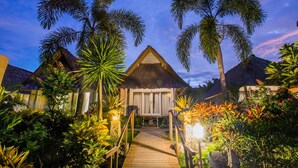 A resort with thatched-roof cottages, a wooden pathway, and tropical vegetation.
