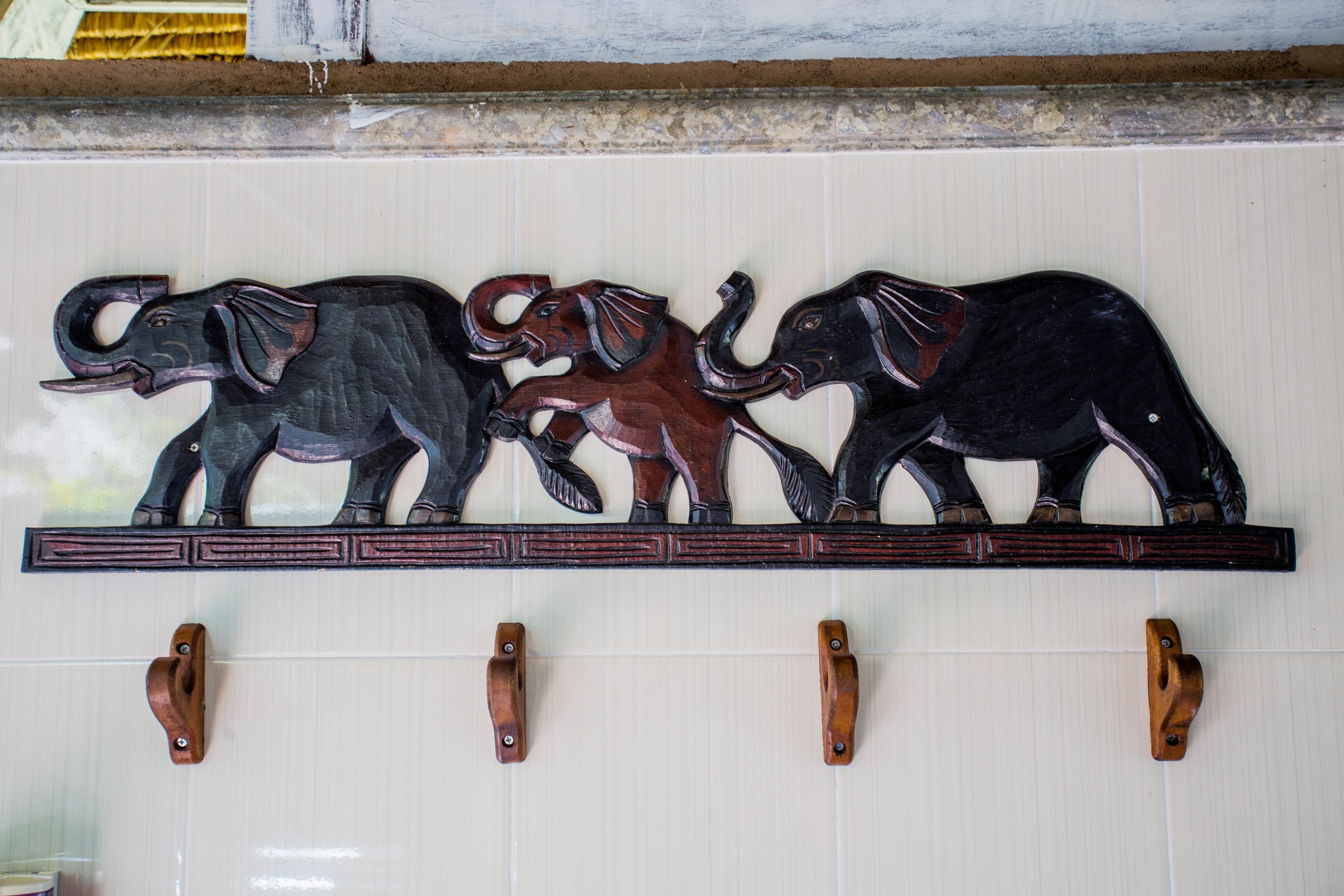 A wall-mounted shelf with three wooden elephant sculptures.