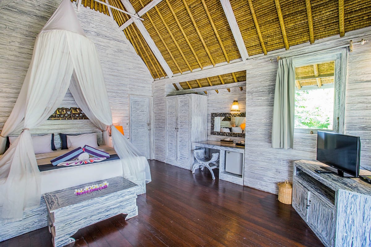 Una habitación con cama con dosel, televisión, una mesita y una ventana con cortinas.