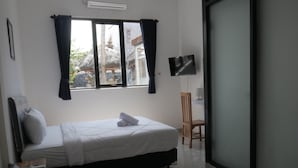 Un dormitorio con una cama, televisión, una silla y un ventanal con cortinas.