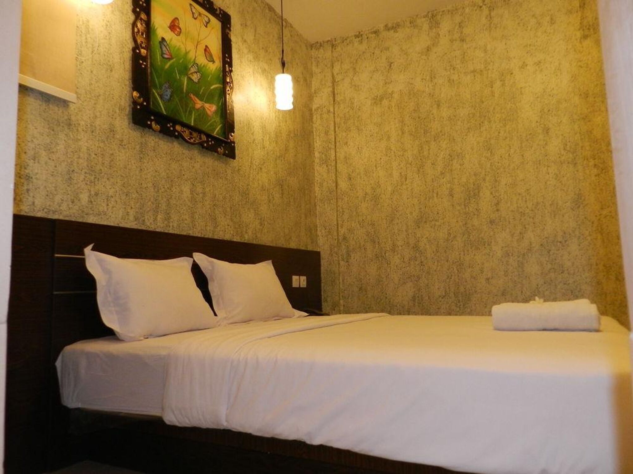 Une chambre d’hôtel avec un lit, du linge de lit blanc, un tableau encadré au mur et un luminaire suspendu.