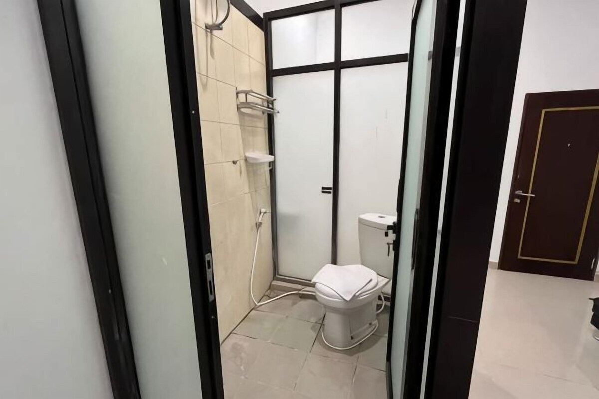 A compact bathroom with a shower, toilet, and a small storage shelf.