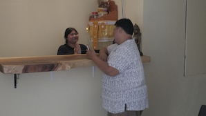 Un área de recepción con un mostrador de madera, un estante en la pared con varios objetos y una estatua.