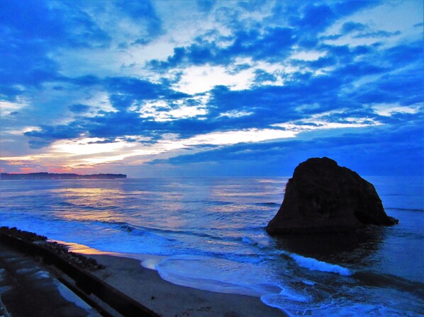 A coastal scene with a large rock formation, calm sea, and a clear sky.