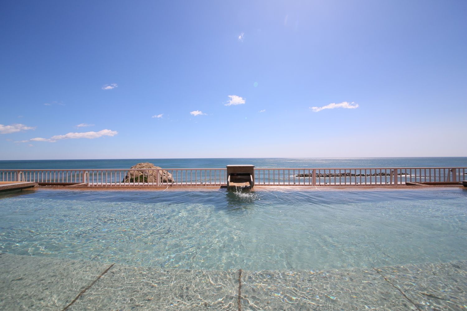A clear pool with a view of the sea and a rocky outcrop in the background.