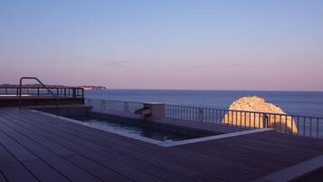 A wooden deck with a pool and a view of the sea.