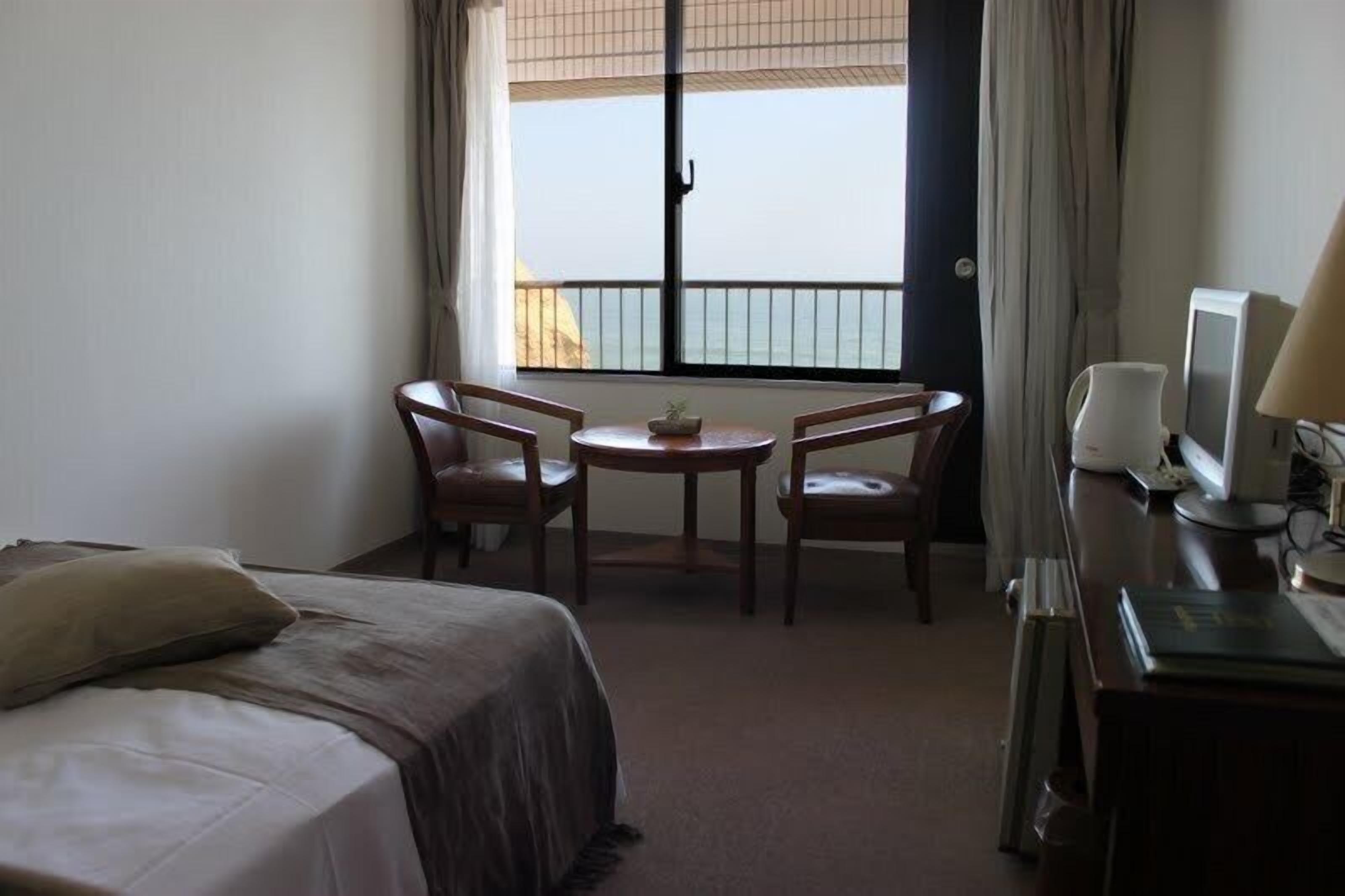 Una habitación de hotel con una cama, una pequeña mesa redonda con dos sillas, una televisión y una ventana con vista al mar.
