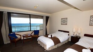 Habitación de hotel con dos camas, una silla, una mesita y vista al océano.