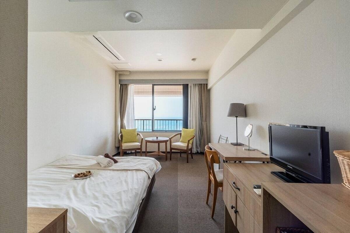 Hotelkamer met een bed, een bureau met een televisie, een stoel, een klein tafeltje en een balkon met uitzicht.