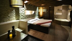 A modern hotel room with a stone wall, a large bed, a sitting area, and a separate bathroom with a bathtub. - Victoria Court Suites - Pasig (Pasig)