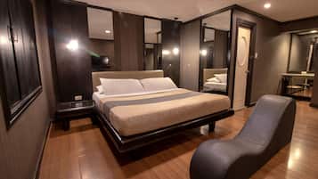 A modern hotel room with a large bed, a seating area, a mirror, and a small desk.