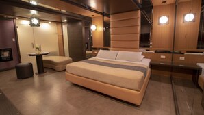 A modern hotel room with a large bed, a small round table, a sofa, and a mirror. - Victoria Court San Fernando - Pampanga (San Fernando)