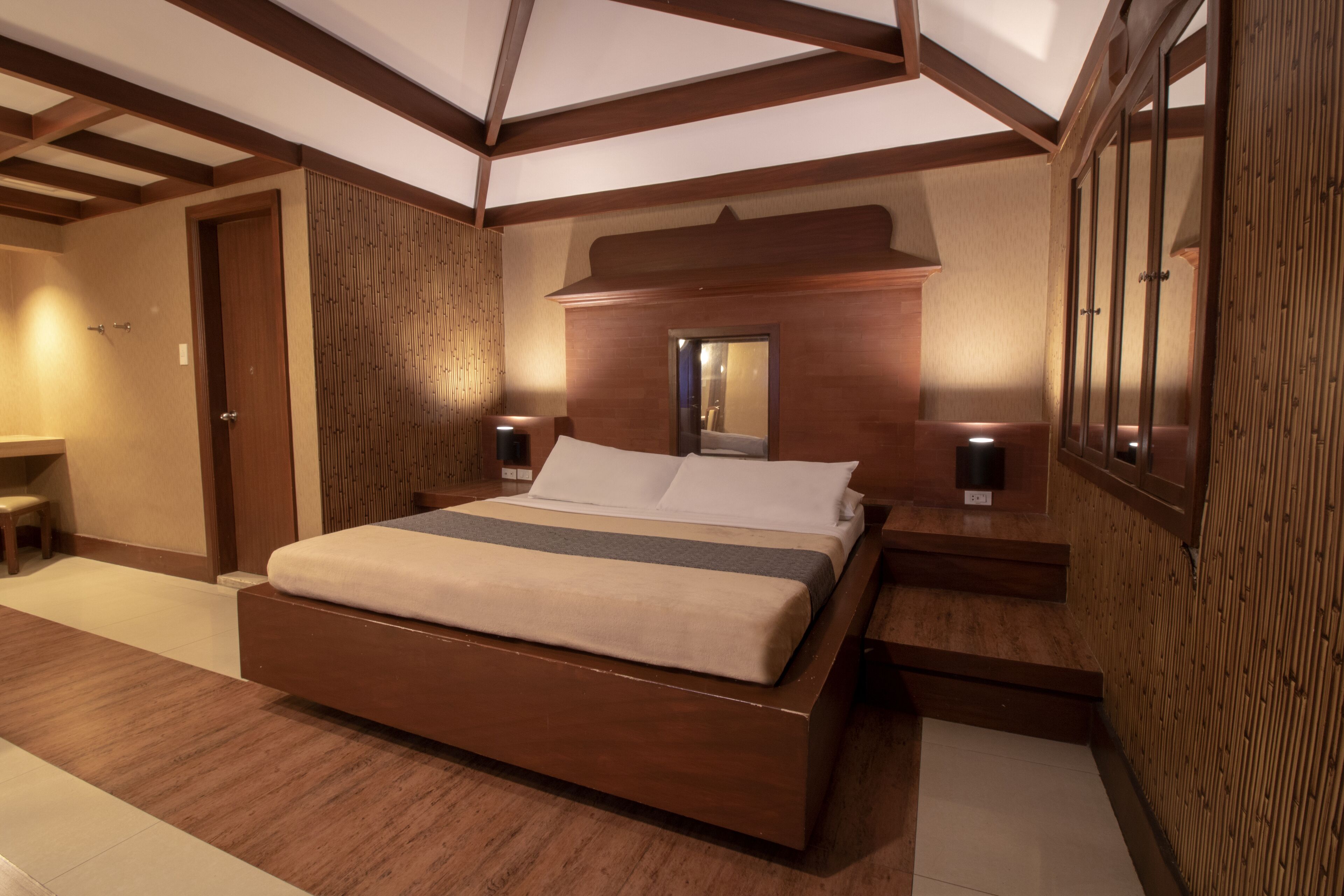 Un dormitorio moderno con una cama grande, cabecera de madera y un espejo encima.