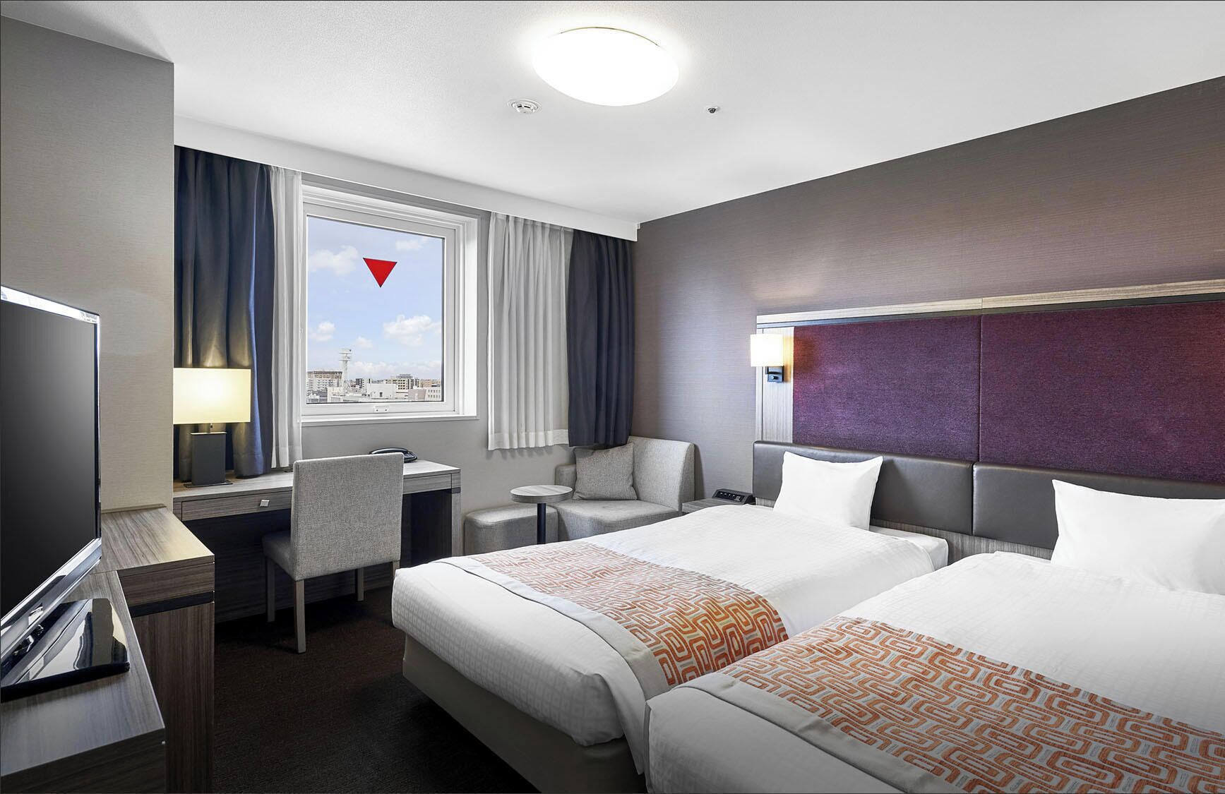 Une chambre d’hôtel avec deux lits, un bureau, une chaise, une télévision et une fenêtre donnant sur la ville.