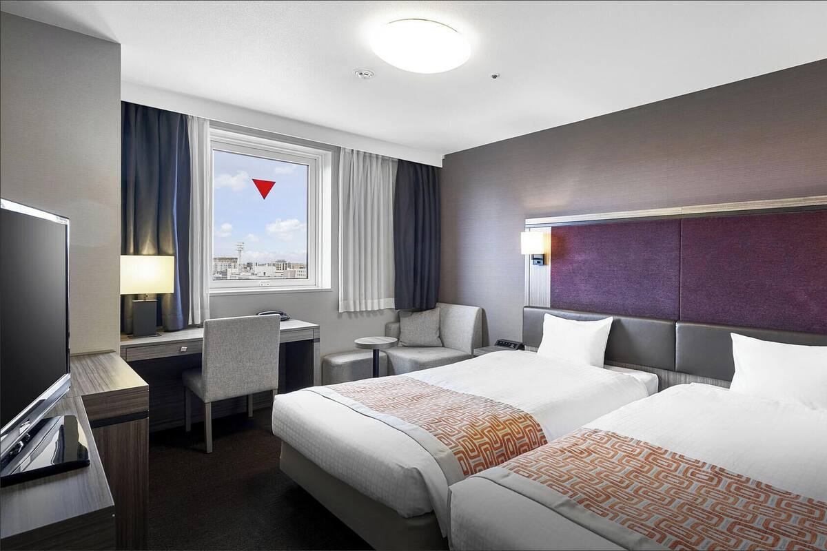 Une chambre d’hôtel avec deux lits, un bureau, une chaise, une télévision et une fenêtre donnant sur la ville.