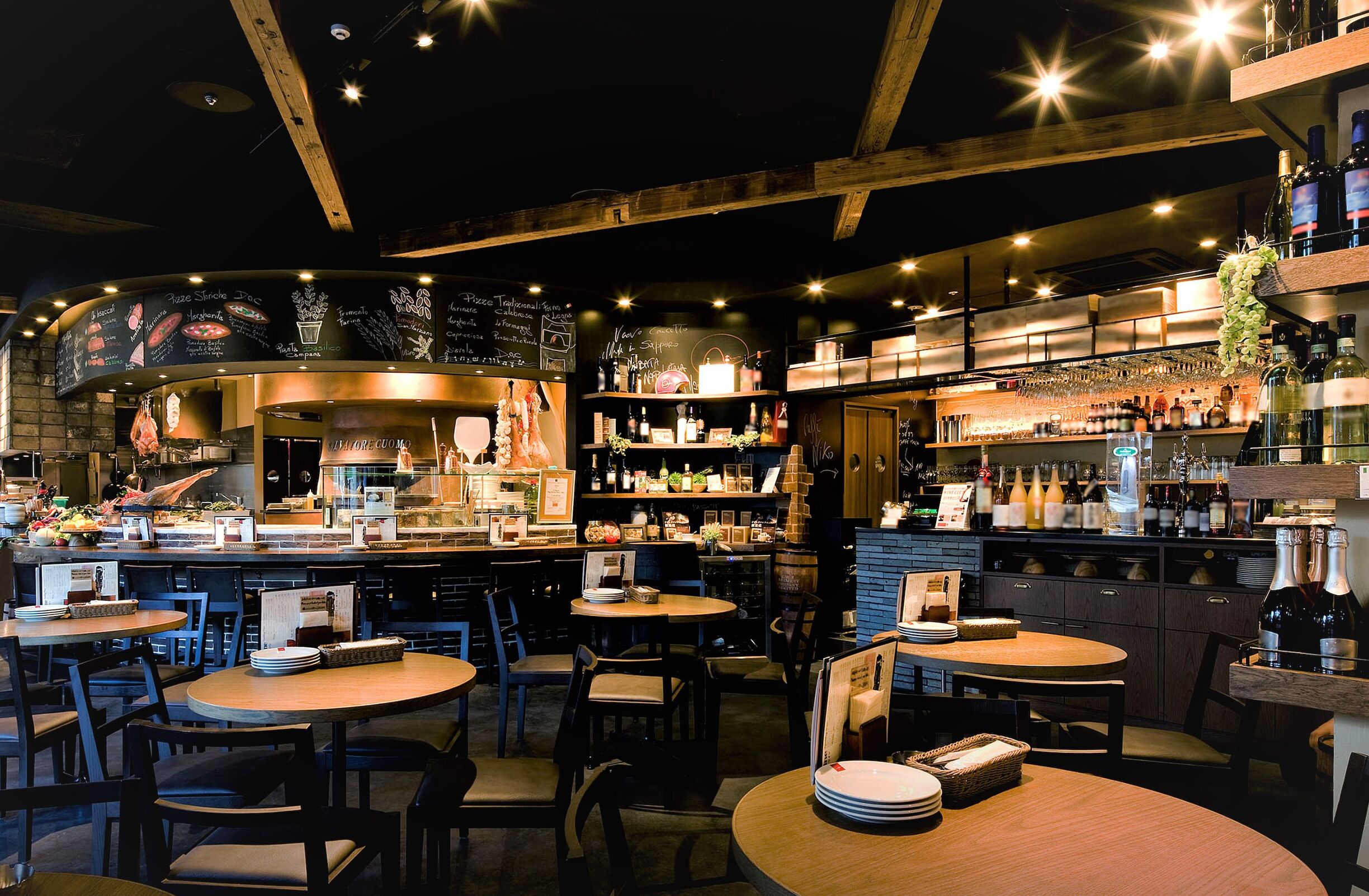 Een restaurant met ronde tafels, stoelen, een bar met flessenrekken en een krijtbordmenu.