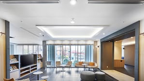 A modern hotel lobby with a sofa, ottomans, a TV, and a bookshelf. - Daiwa Roynet Hotel Sapporo Susukino (Sapporo)