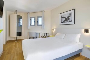 Habitación de hotel con una cama grande, un escritorio, una silla y un cuadro en la pared.