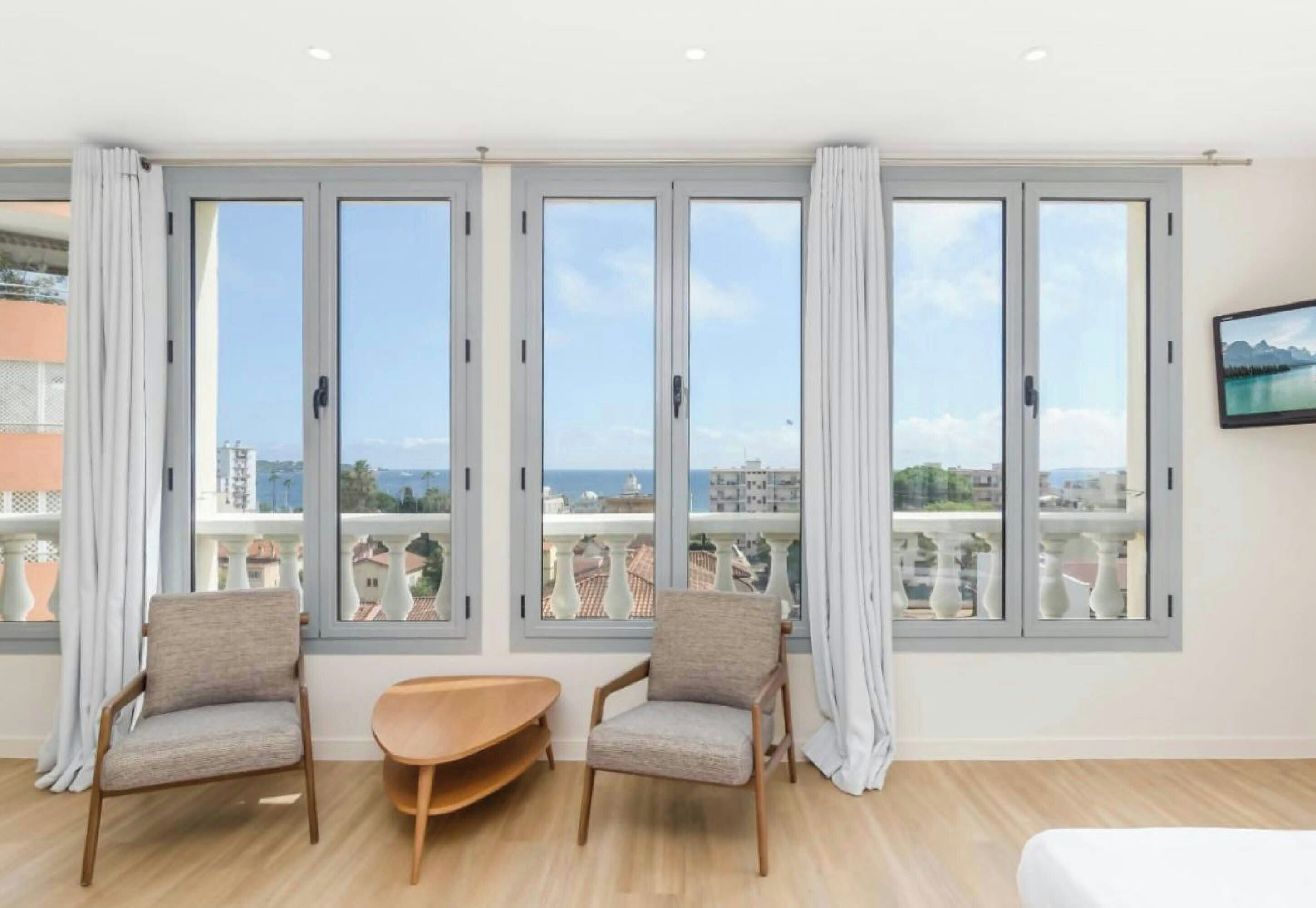 Habitació d'hotel amb balcó, dos seients còmodes, una taula petita i un televisor fixat a la paret.