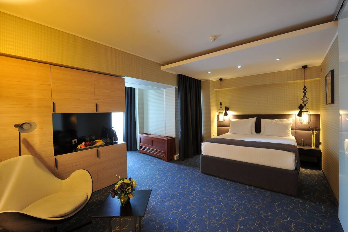 A hotel room with a bed, bedside table, lamp, chair, and a desk with a vase of flowers.