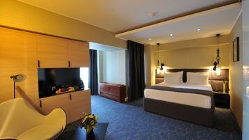Ein Hotelzimmer mit Bett, Nachttisch, Lampe, Sessel und Schreibtisch mit Blumenvase.