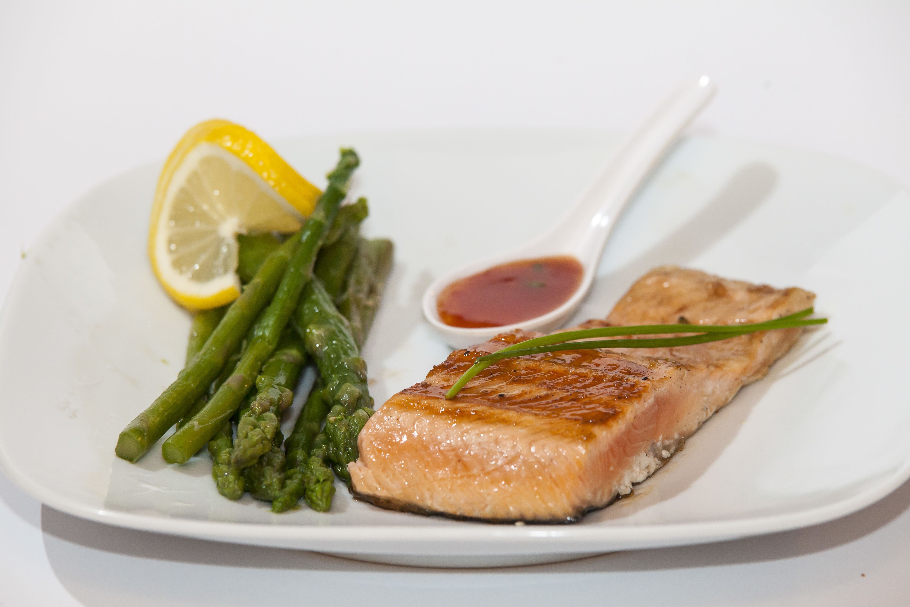 A plate with grilled salmon, asparagus, a lemon wedge, and a small bowl of sauce.