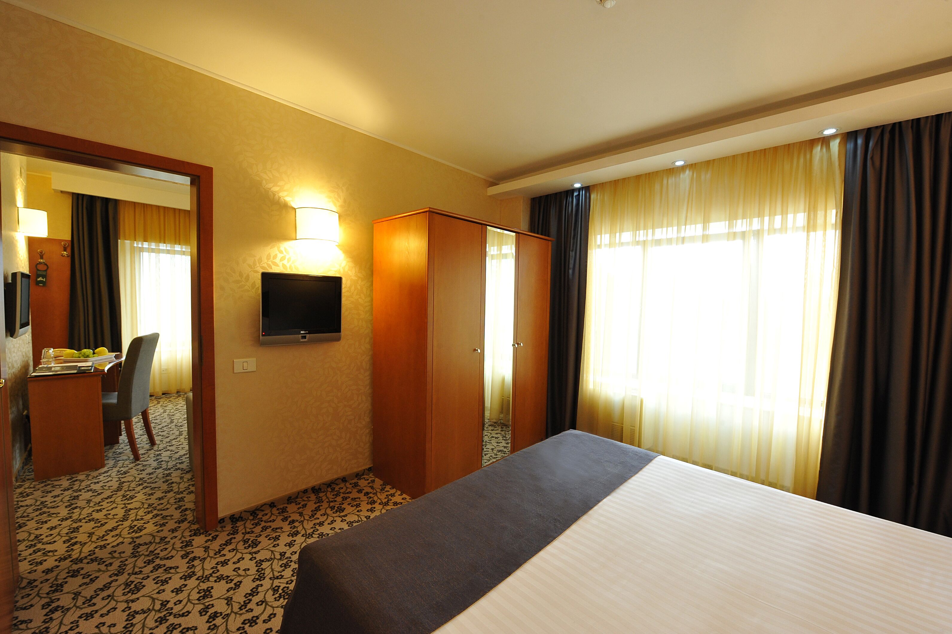 A hotel room with a bed, a desk with a chair, a television, and a wardrobe.