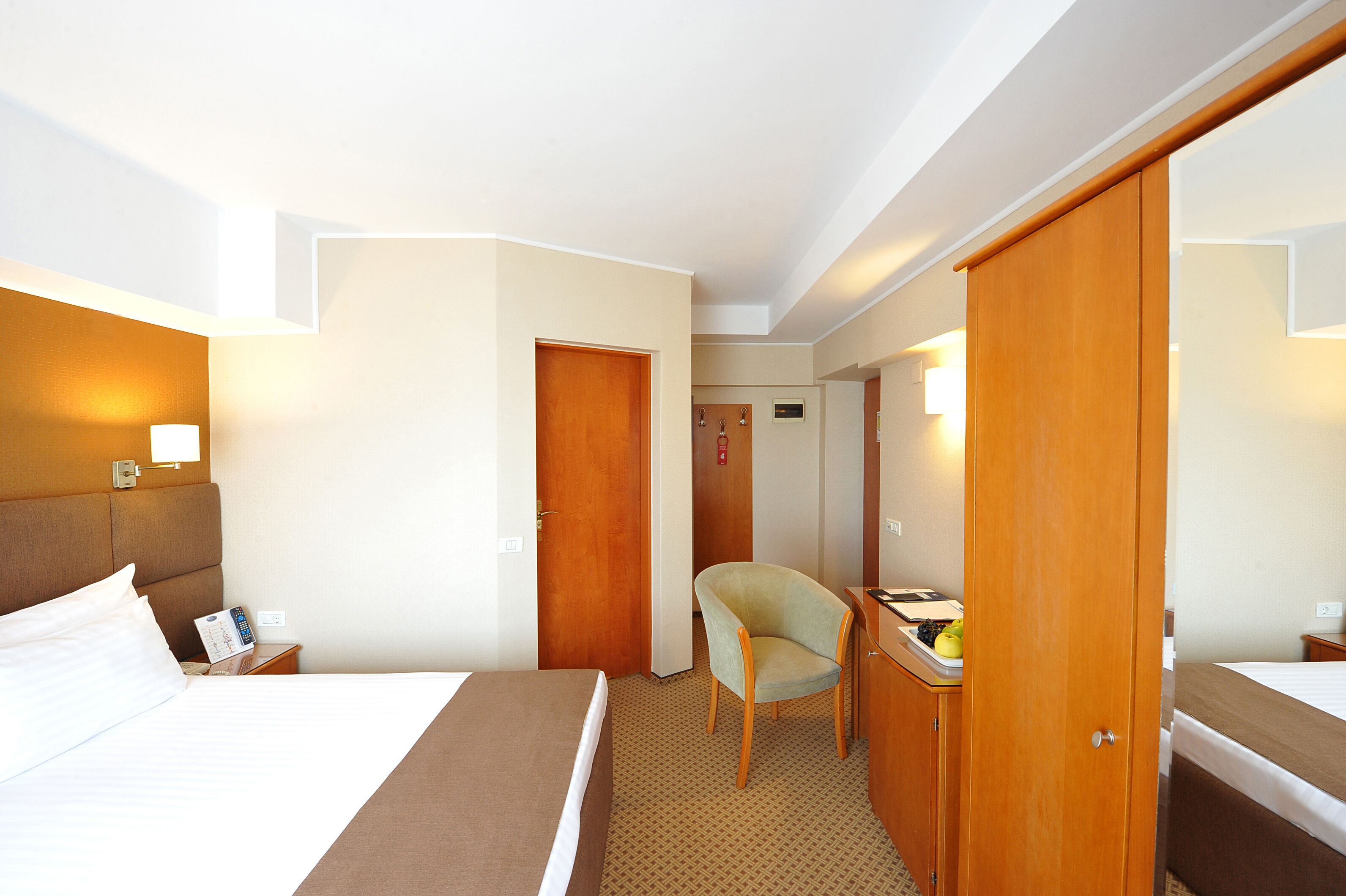 A hotel room with a bed, a chair, a desk, and a wardrobe.