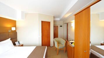 A hotel room with a bed, a chair, a desk, and a wardrobe.