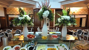 Montaje de bufé con diversos alimentos, como frutas, verduras y pasteles, dispuestos sobre una mesa de vidrio con jarrones decorativos.