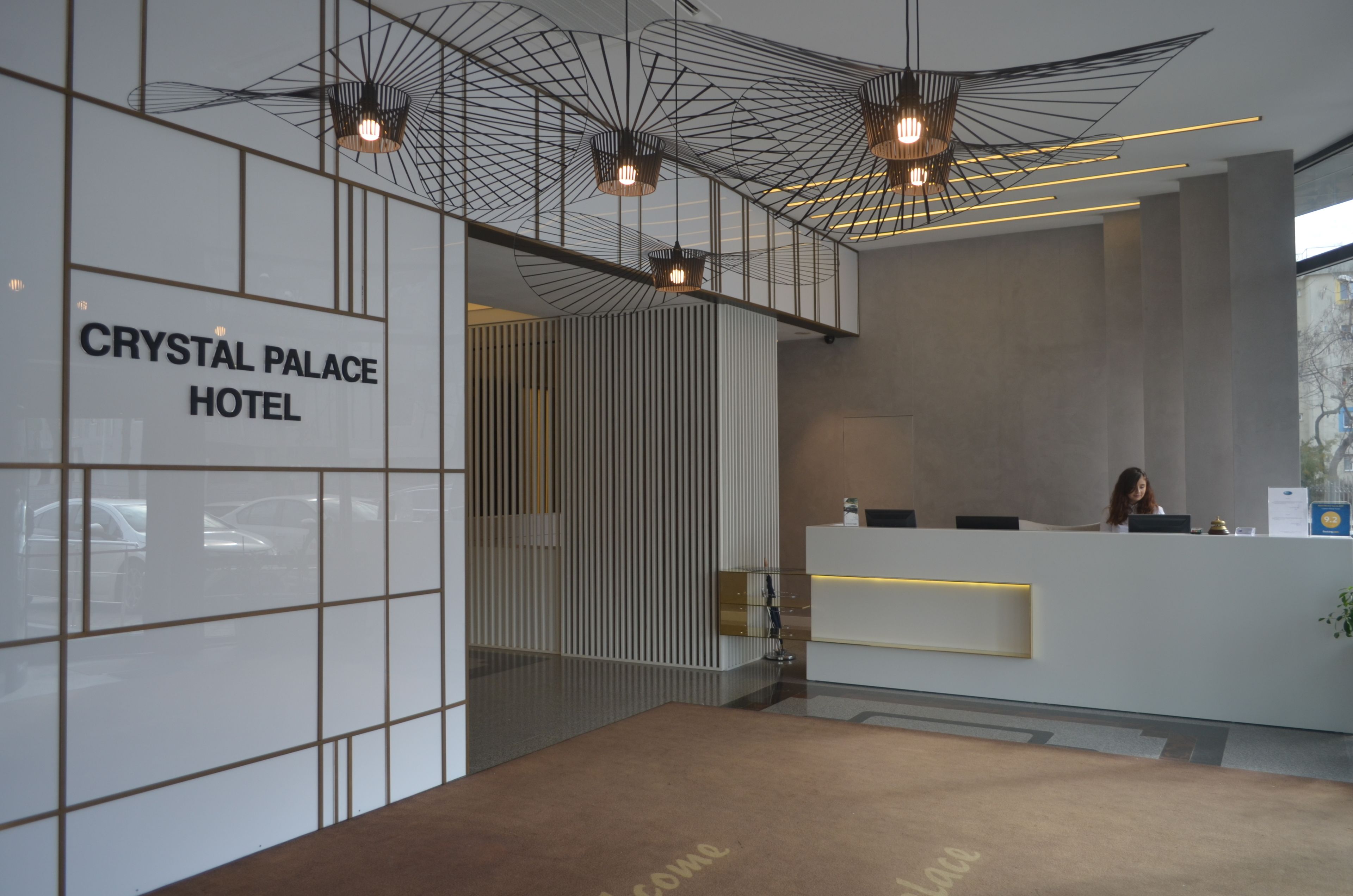 A modern hotel reception area with a glass partition, a reception desk, and a sign reading "CRYSTAL PALACE HOTEL".