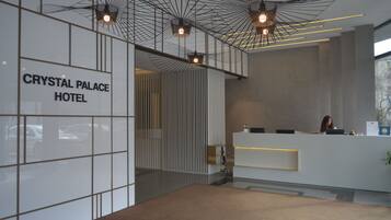 A modern hotel reception area with a glass partition, a reception desk, and a sign reading "CRYSTAL PALACE HOTEL".