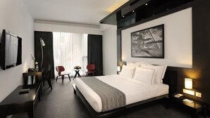 Et moderne hotelværelse med en stor seng, et skrivebord, en stol, et fjernsyn og et billede på væggen.