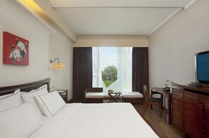 A hotel room with a bed, a desk, a chair, a TV, and a window with curtains. - Escape Hotel & Spa (Bengaluru)
