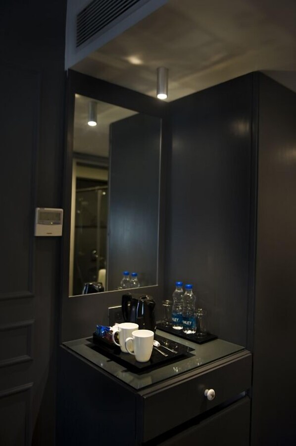 A modern bathroom with a dark color scheme, a large mirror, a coffee machine, and two bottles of water.