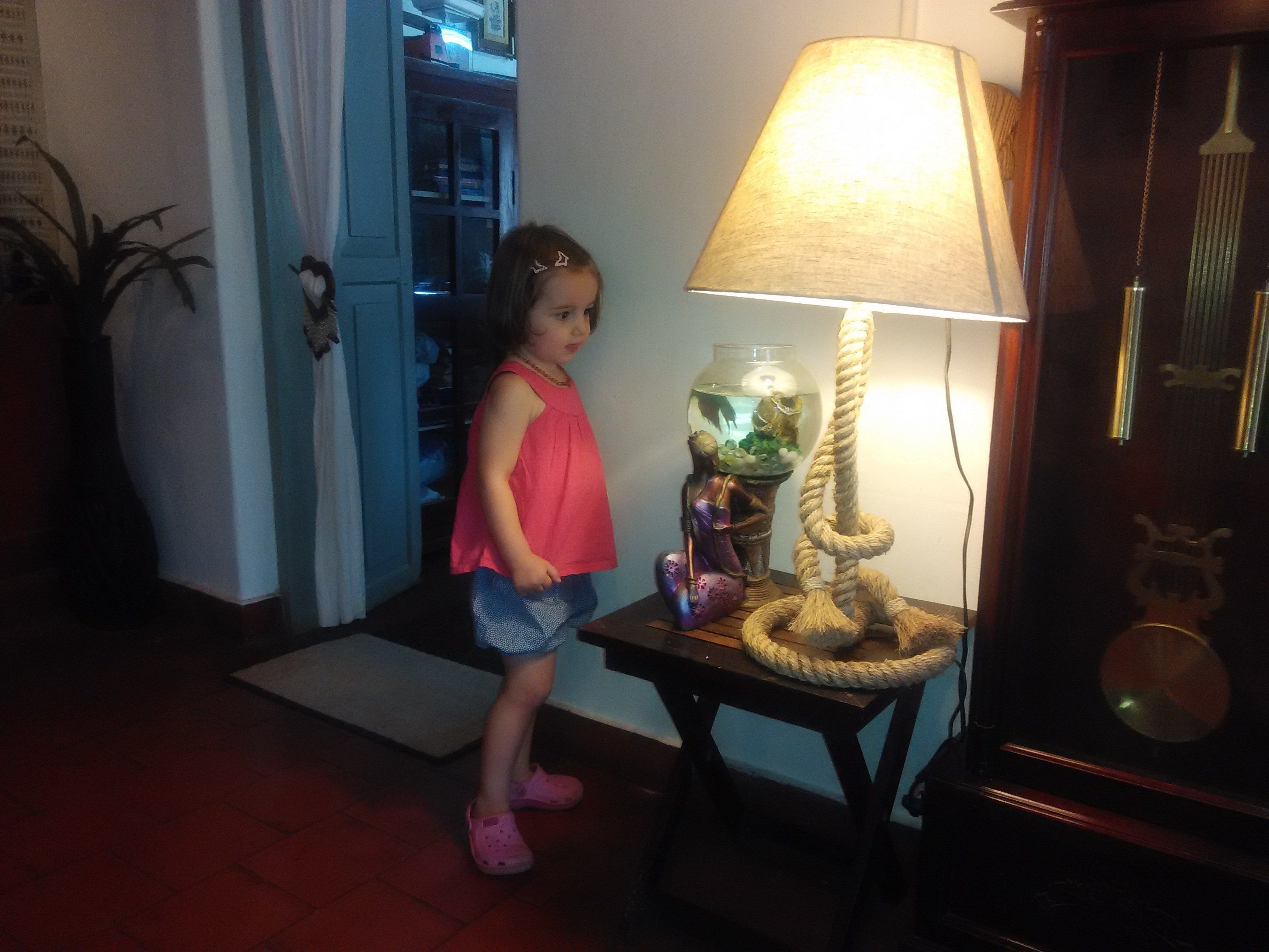 Un niño de pie en un pasillo, con una lámpara y un acuario sobre una mesa.