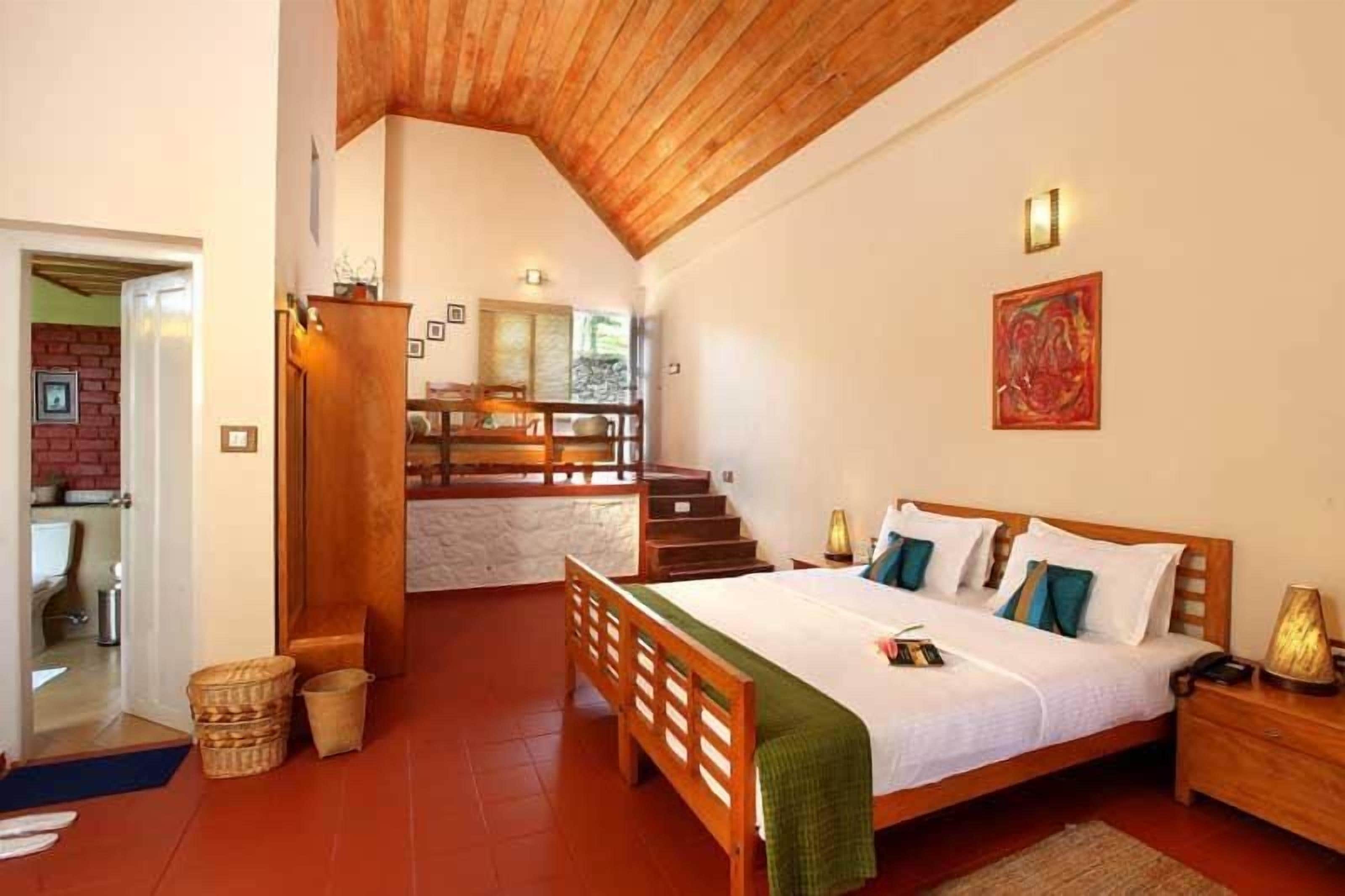 Un dormitorio con cama de madera, una mesita de noche, una manta verde y una escalera que lleva a un nivel superior.