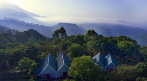 Un paysage de montagne avec deux bâtiments coiffés de toits hexagonaux, entourés d’une forêt dense.