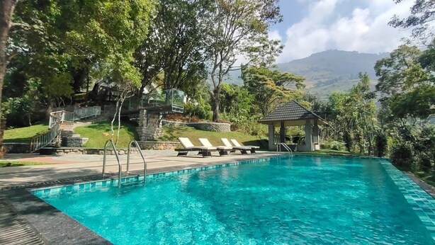 A clear blue pool with steps leading up to a gazebo, surrounded by lush greenery and a mountainous backdrop. - Ambady Estate (Devikolam)