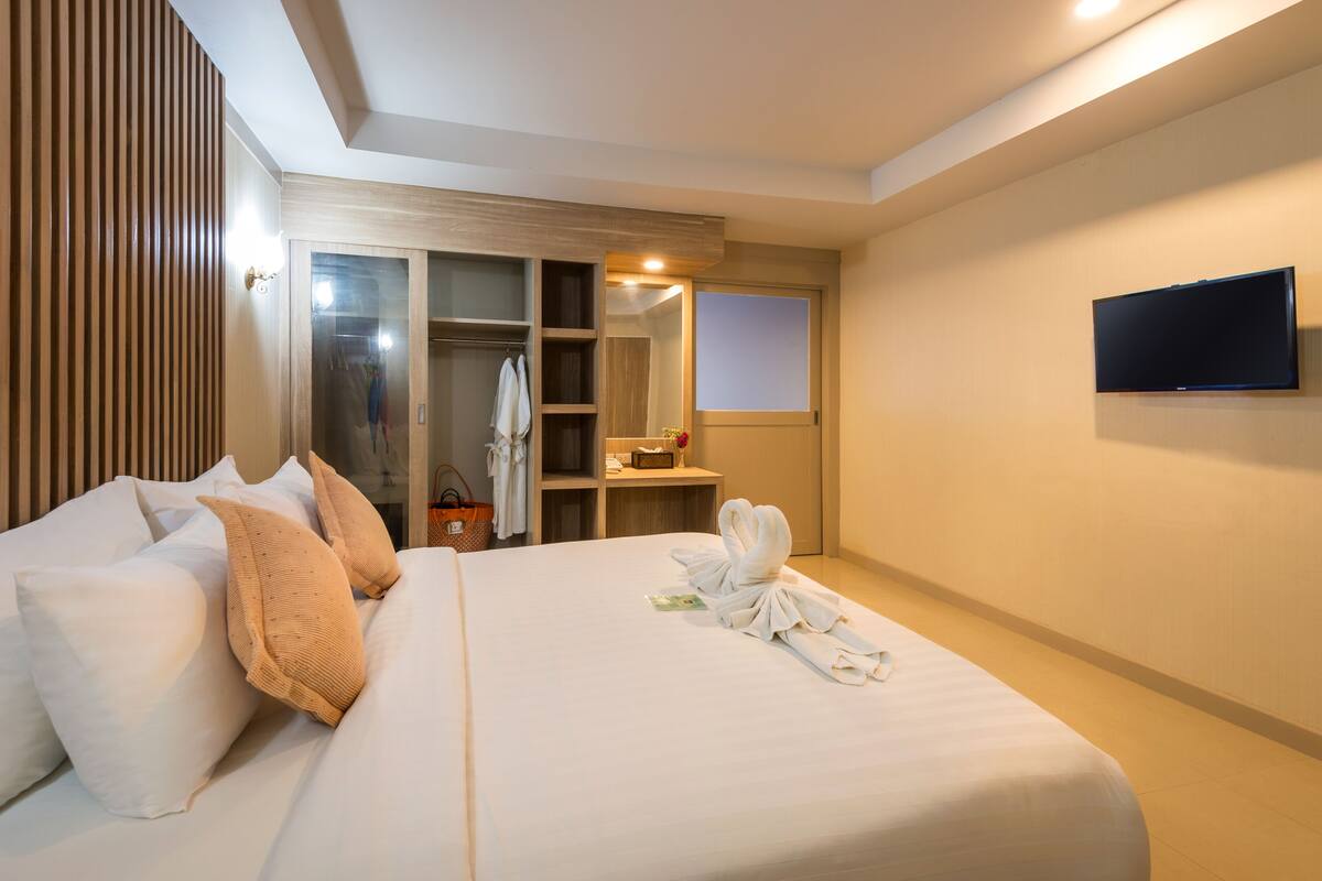 A hotel room with a large bed, a wardrobe, a mirror, and a flat-screen TV.