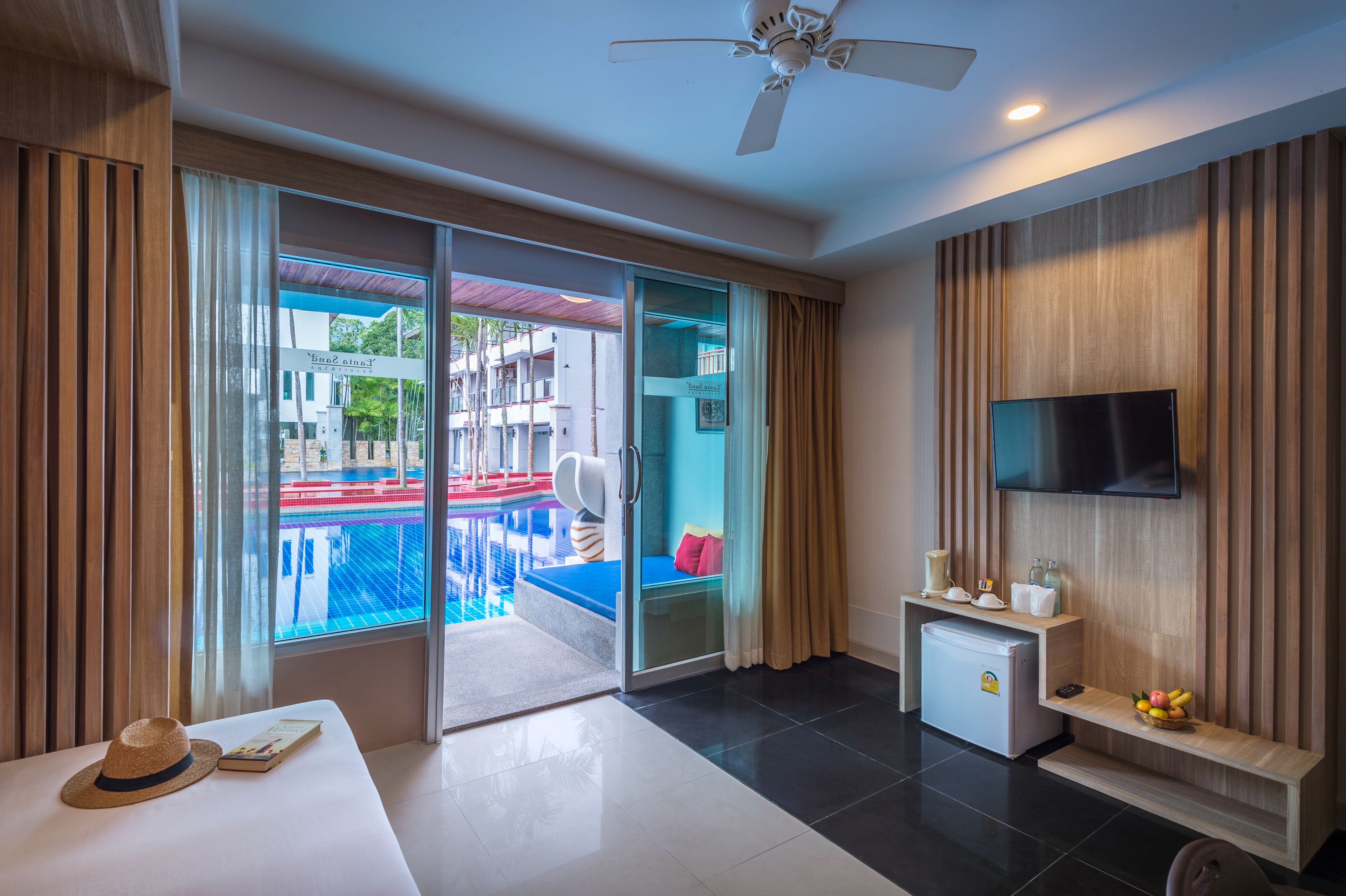 Ein modernes Hotelzimmer mit Balkon, Flachbildfernseher, einer Minibar und einem Essbereich mit Blick auf den Pool.