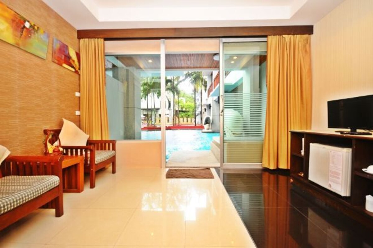 A hotel room with a sofa set, a television, and a view of a pool and outdoor area.