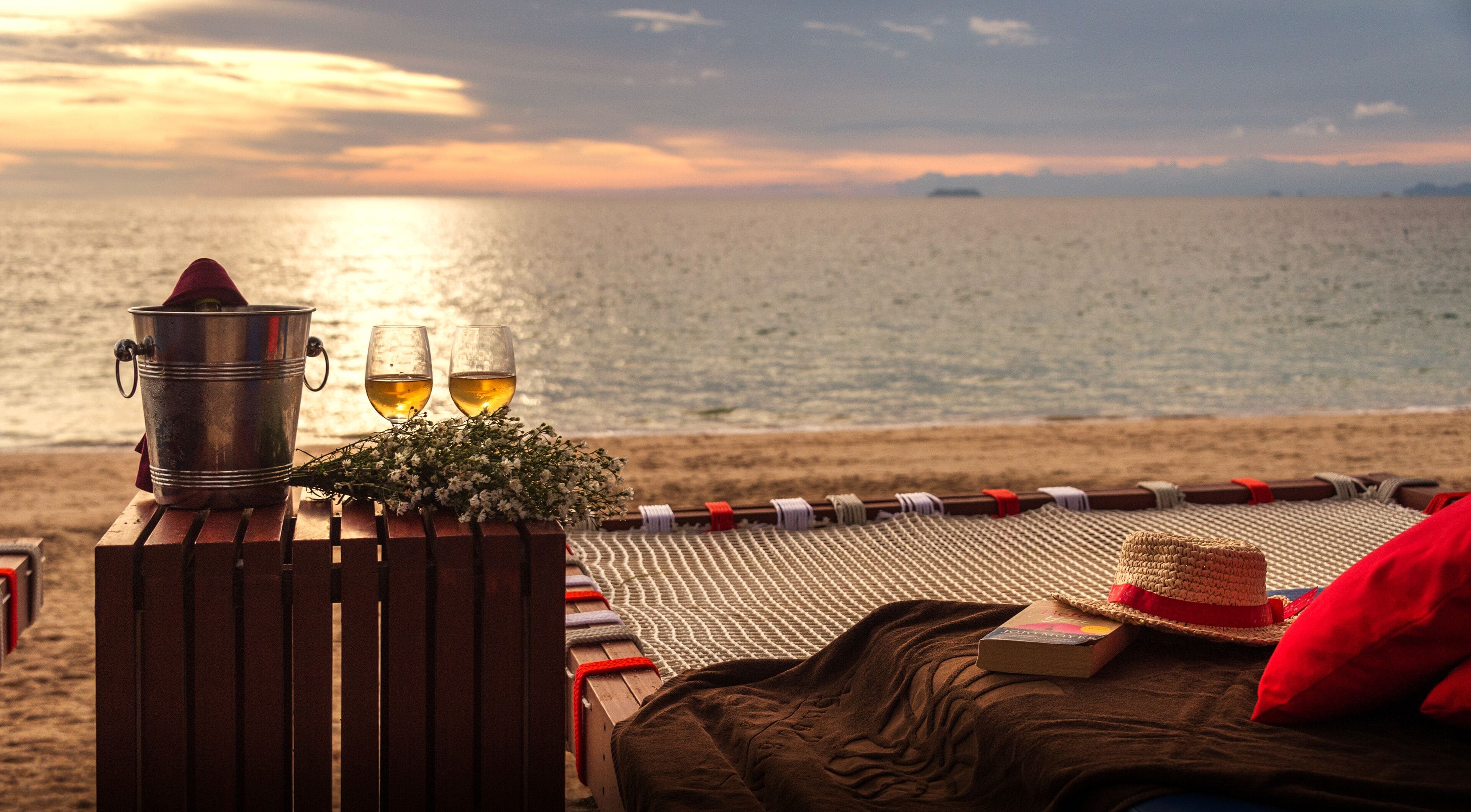 Un entorno frente al mar con un cubo de metal, dos copas de vino y un ramo de flores sobre un banco de madera.