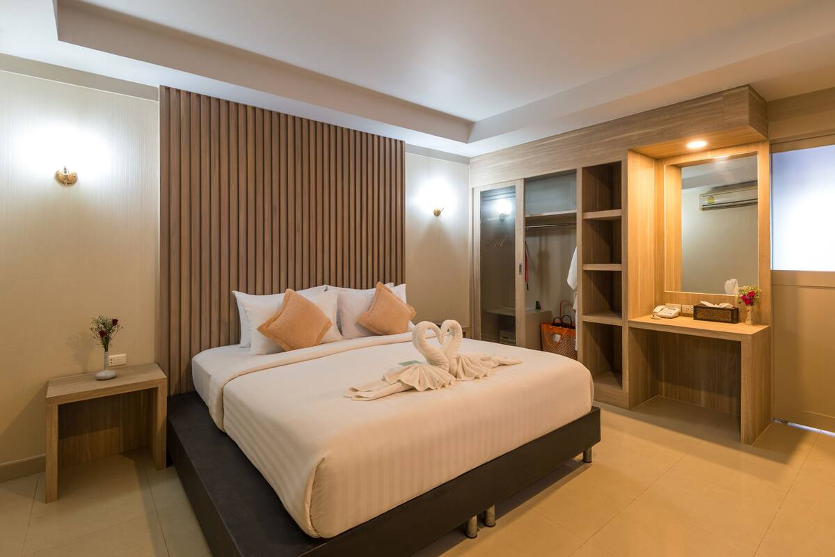 A modern hotel room with a large bed, wooden panel wall, built-in closet, and bedside table with a vase of flowers.