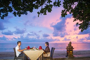 A table set for two at a beachside restaurant with a view of the ocean and a sunset sky. - Lanta Sand Resort & Spa (Ko Lanta)