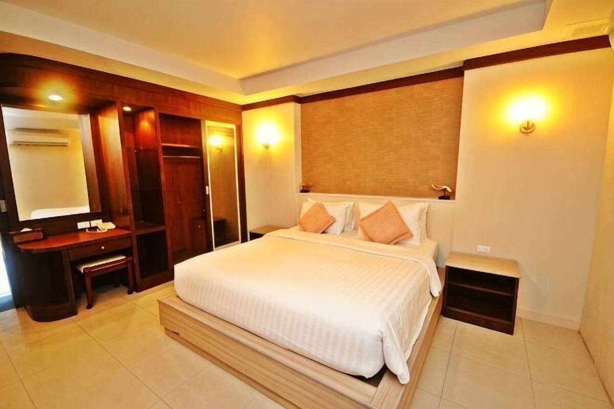 A hotel room with a large bed, a desk, a mirror, and a wardrobe.